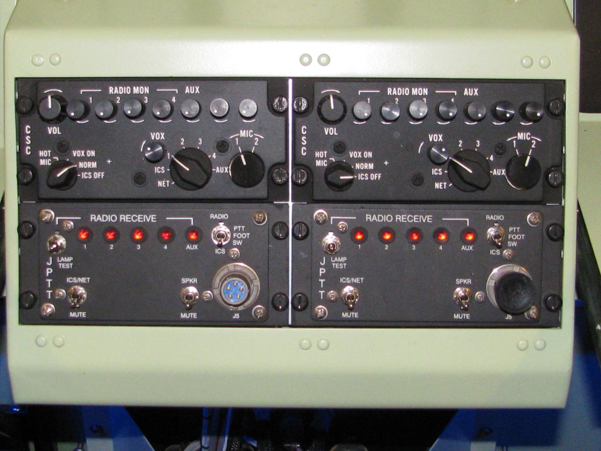 A pair of radio and intercom control panels installed side by side in a console shell, indicator lamps lit during functional testing.